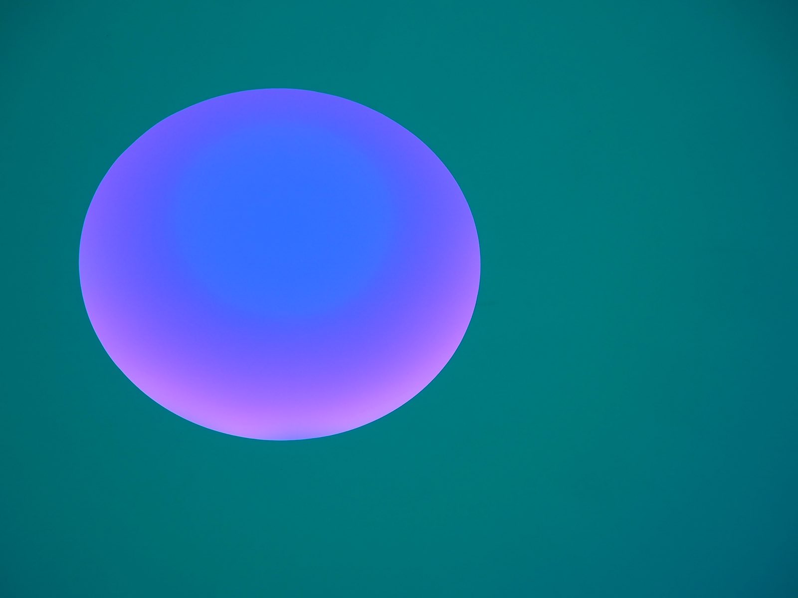 A view from inside James Turrell's C.A.V.U. at Mass MoCA shows a disc of light against a colored field.